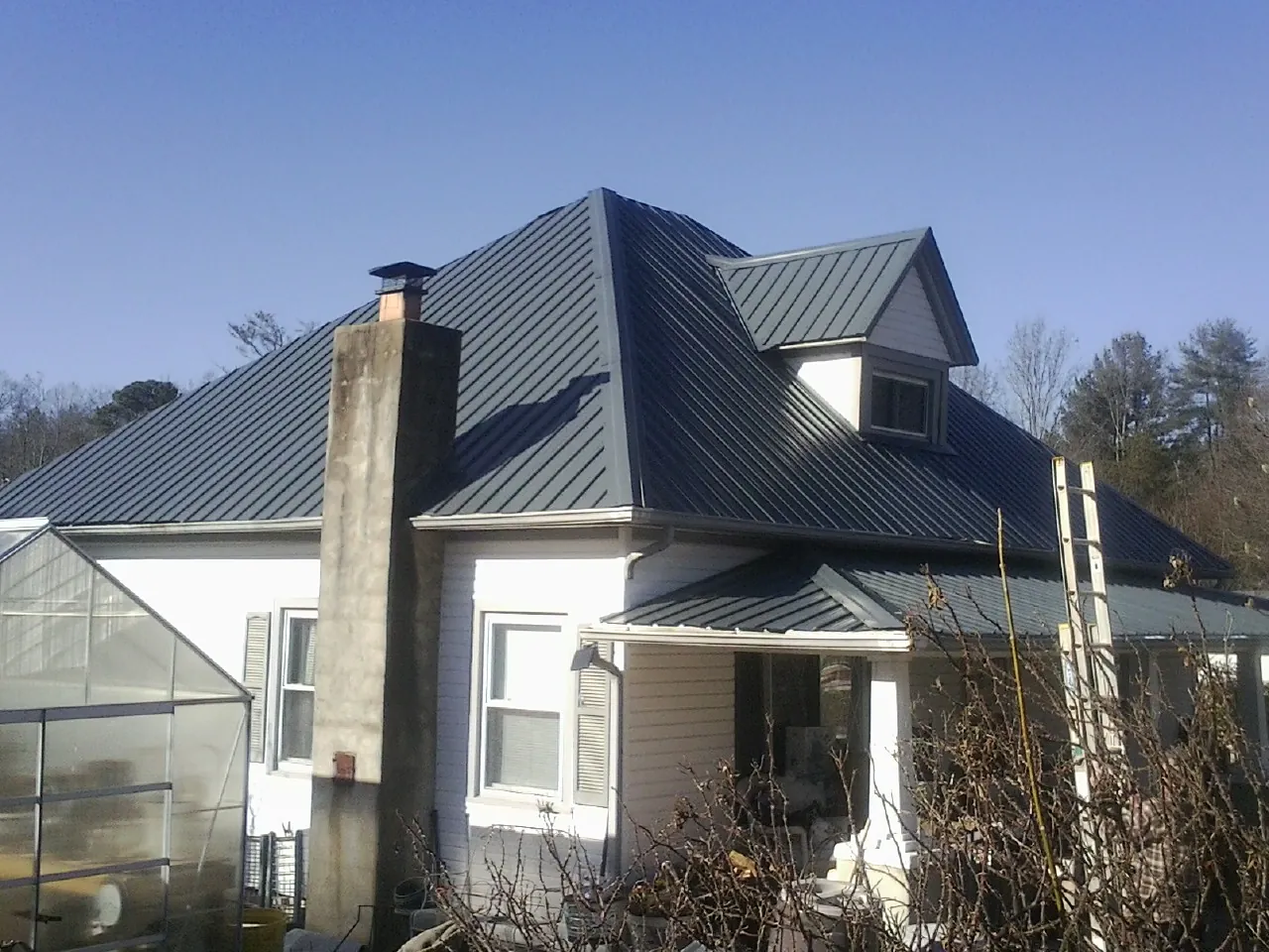 Dark blue standing seam metal roof on a white farmhouse with dormer — Slate & Tile Roof Repair by Roofing Brothers in Amber