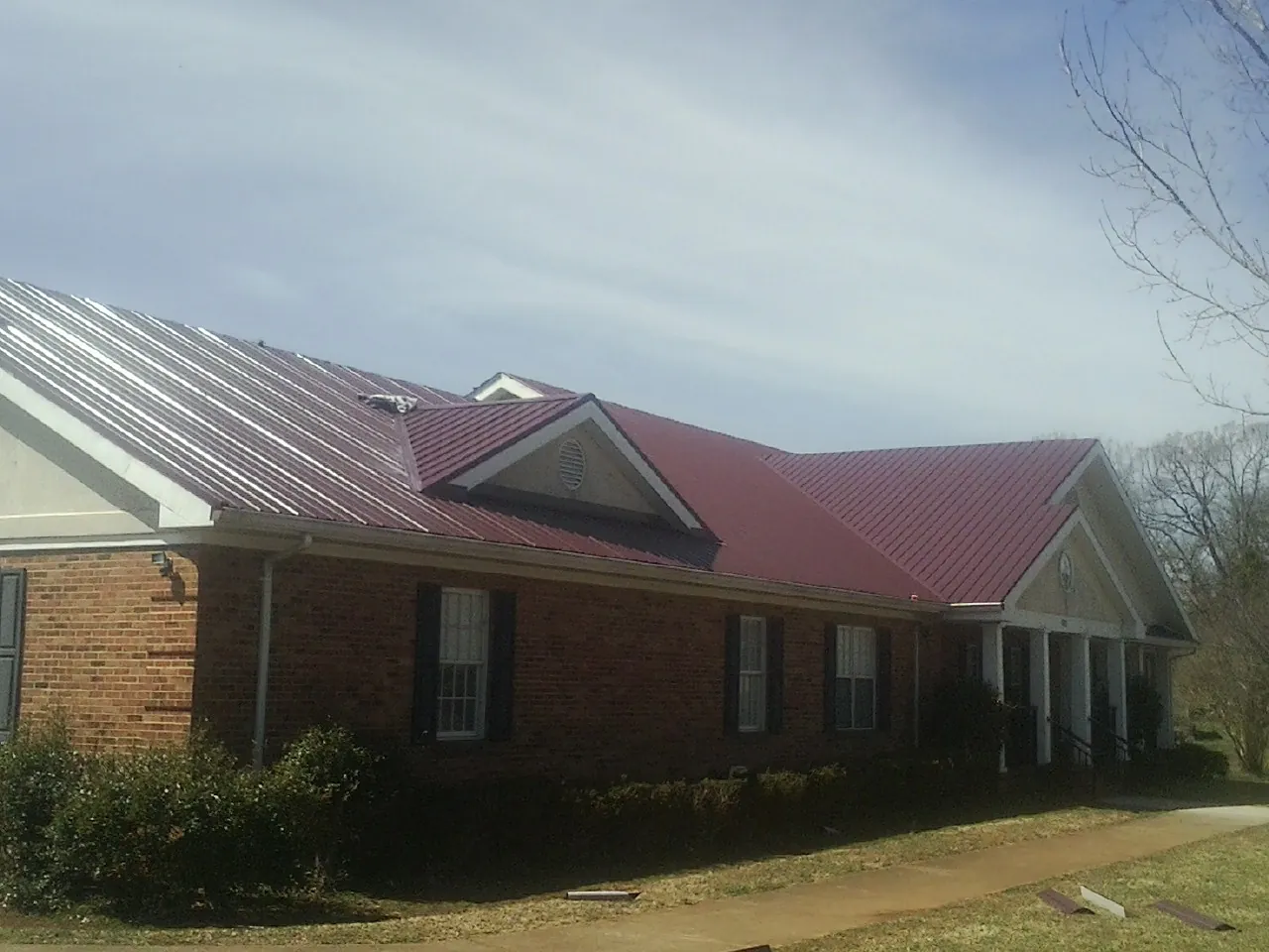 Red metal roof with gabled entries on a long brick building, from a Hail Damage Roof Repair job in Amber
