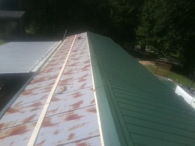 Old rusted panels beside newly installed green metal roofing — Wind Damage Roof Repair by Roofing Brothers in Amber