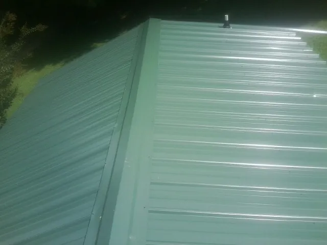 New green metal panels meeting at the ridge of a roof — Flat Roof Repair work by our crew in Amber
