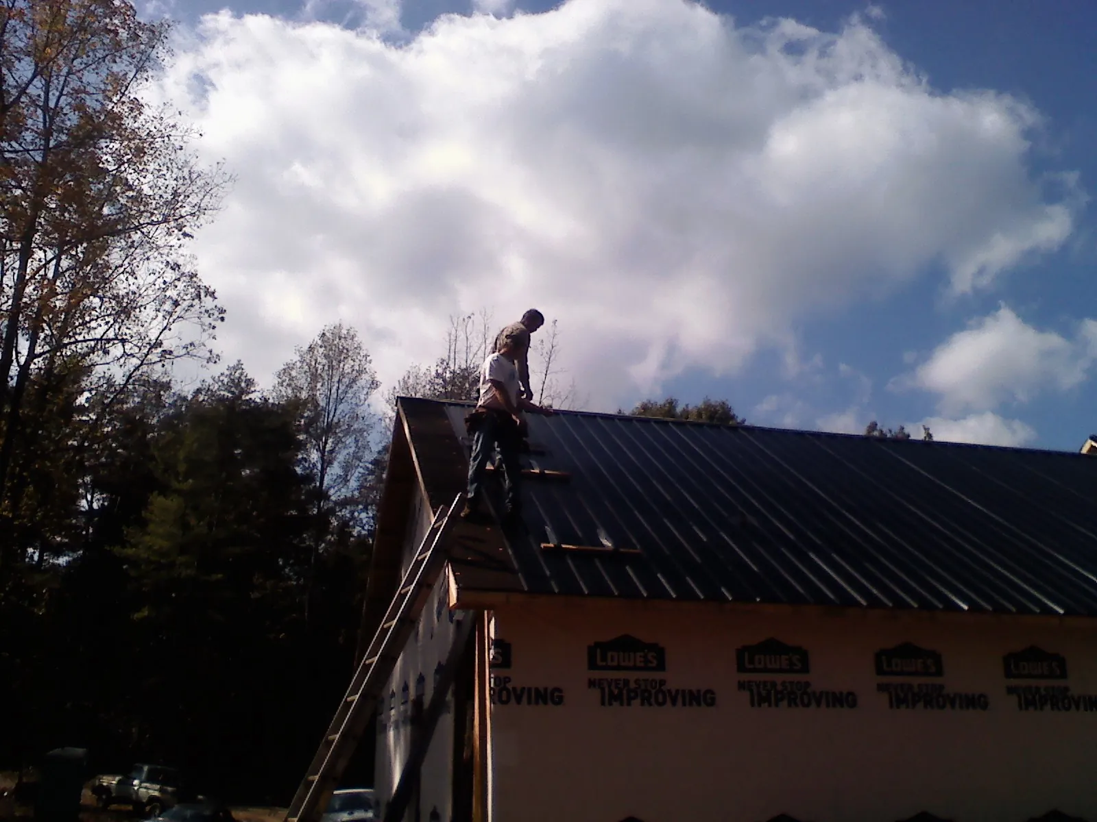 Roofer fastening dark metal panels high against a cloudy sky, from a Roof Inspection job in Amber
