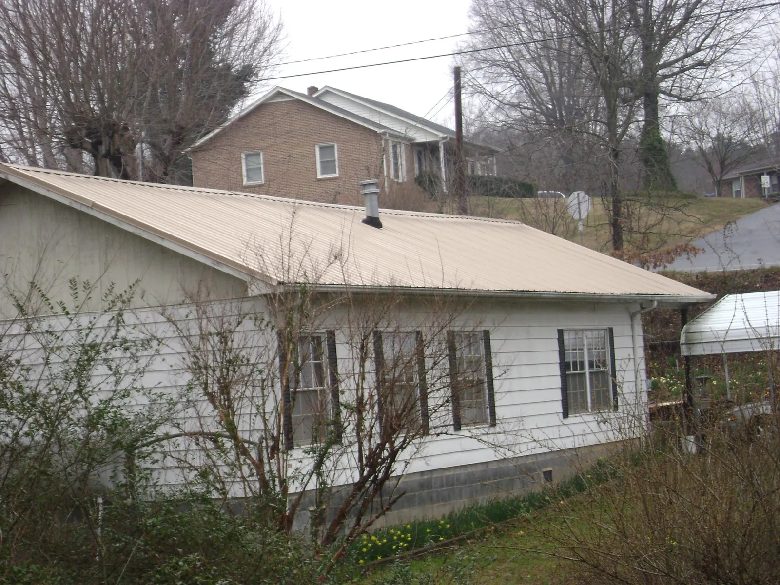 Tan metal roof on a white sided house set into a hillside — Commercial Roofing by Roofing Brothers in Amber