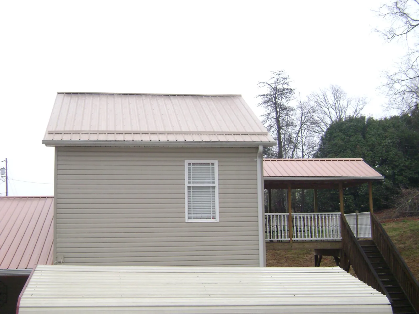 Tan metal roofs on a two story addition and attached porch, from a Roof Replacement job in Amber